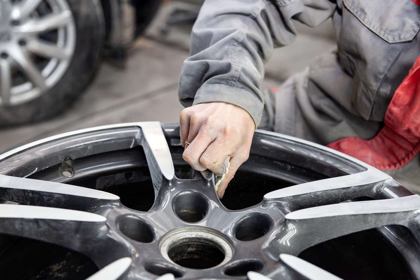 Master body repair man is working on preparing the surface of the aluminum wheel of the car for subsequent painting in the workshop, cleaning and leveling the disk with the help of abrasive material