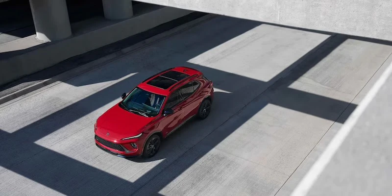 A red 2026 Buick Envision drives along a city street.