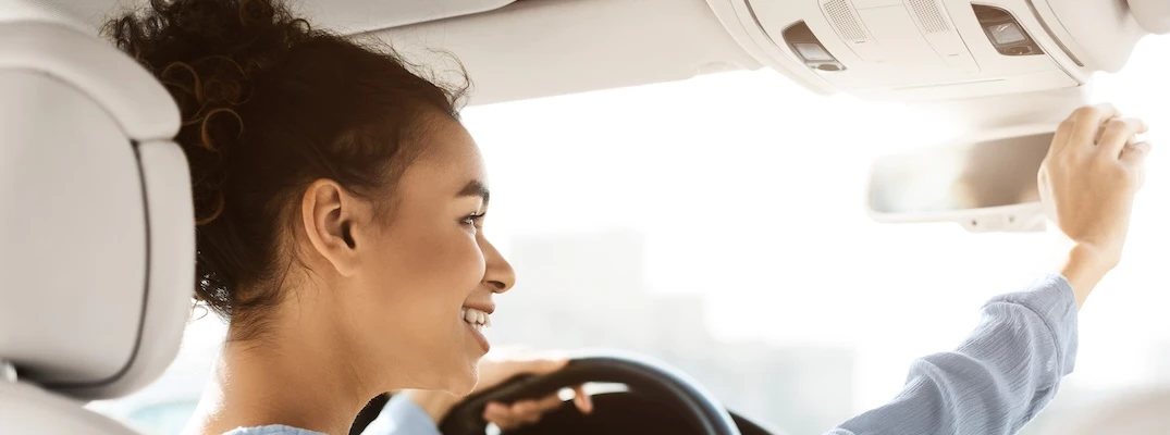 A used car owner repositions the rearview mirror in her car.